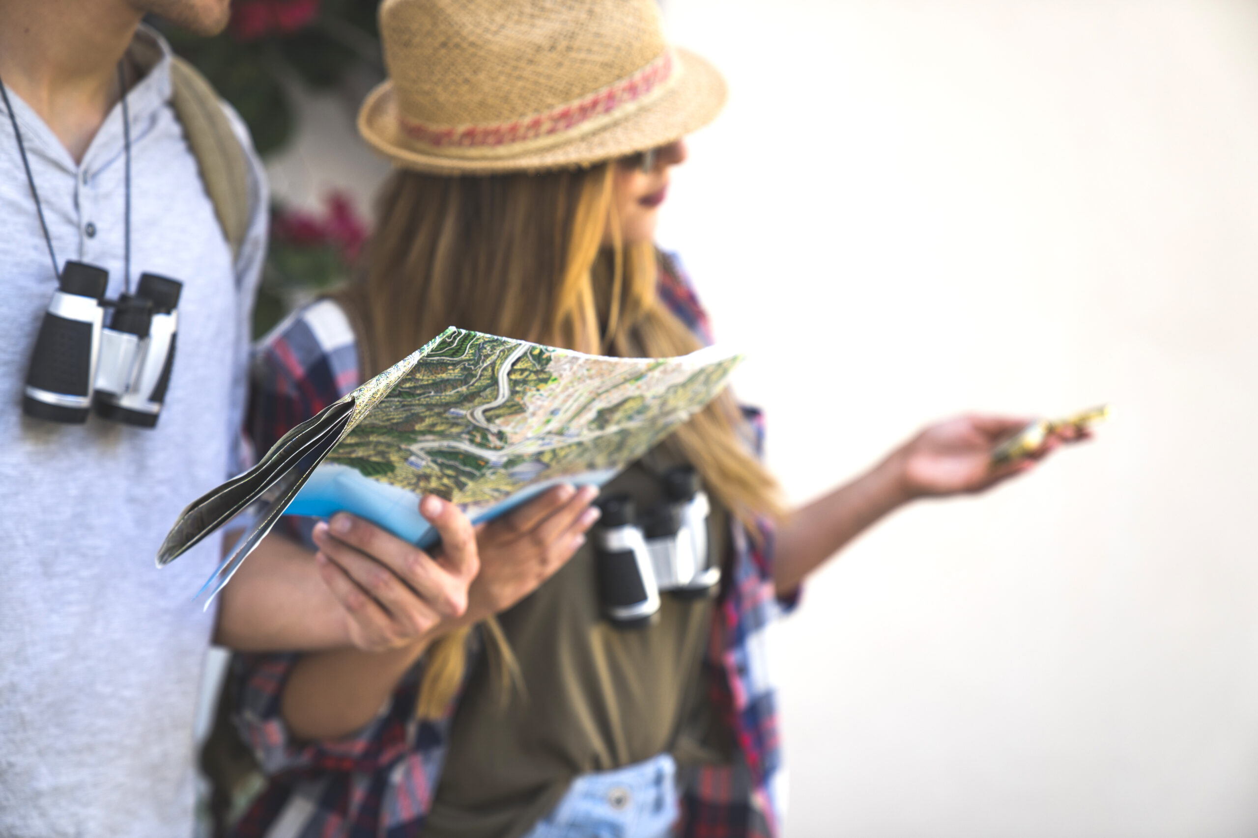 To turister ser på et kart, iført solhatt og ryggsekk. De holder også kikkert, omgitt av blomster.